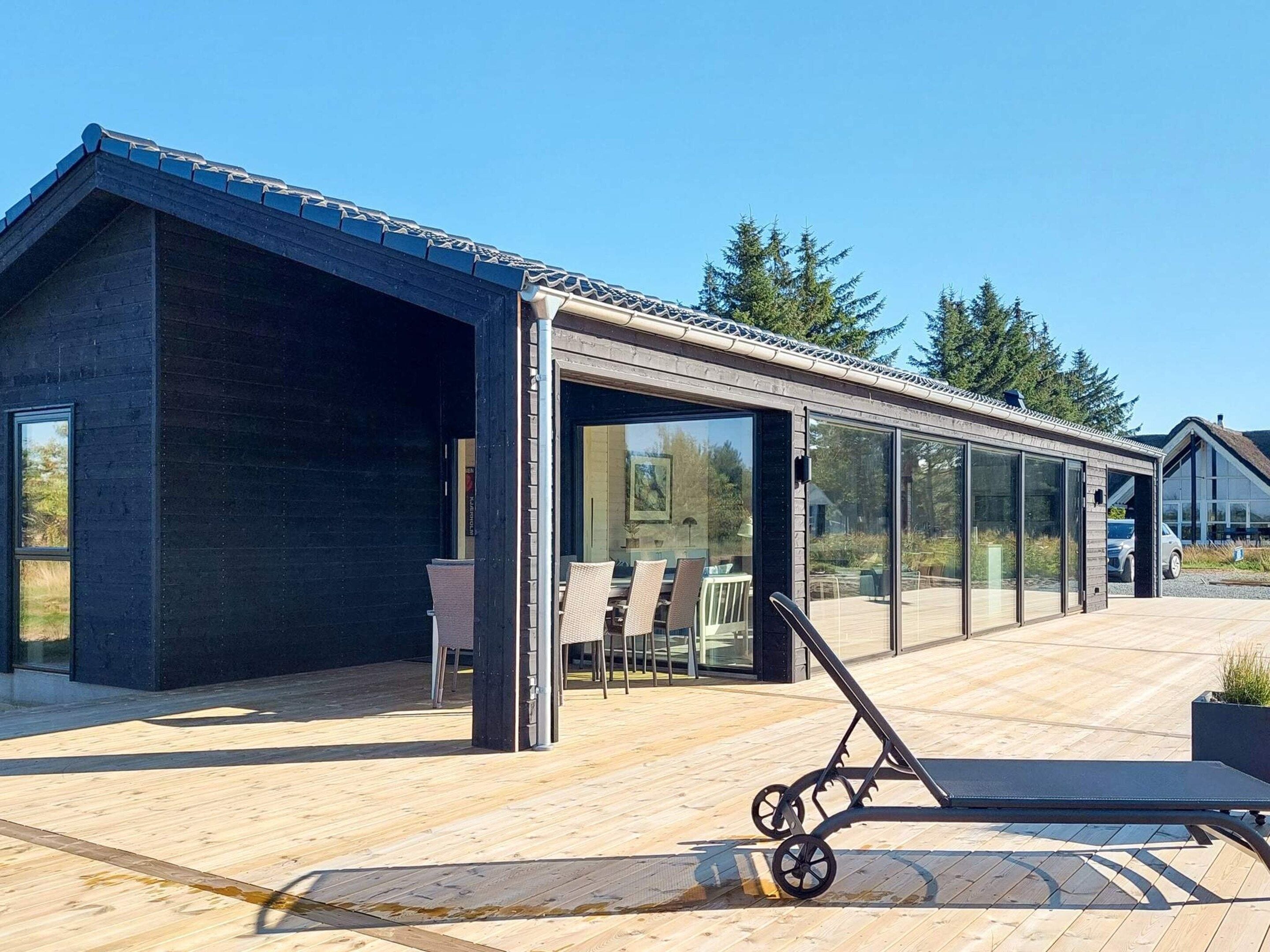 A modern house with a covered outdoor area, a deck, and a lounge chair.
