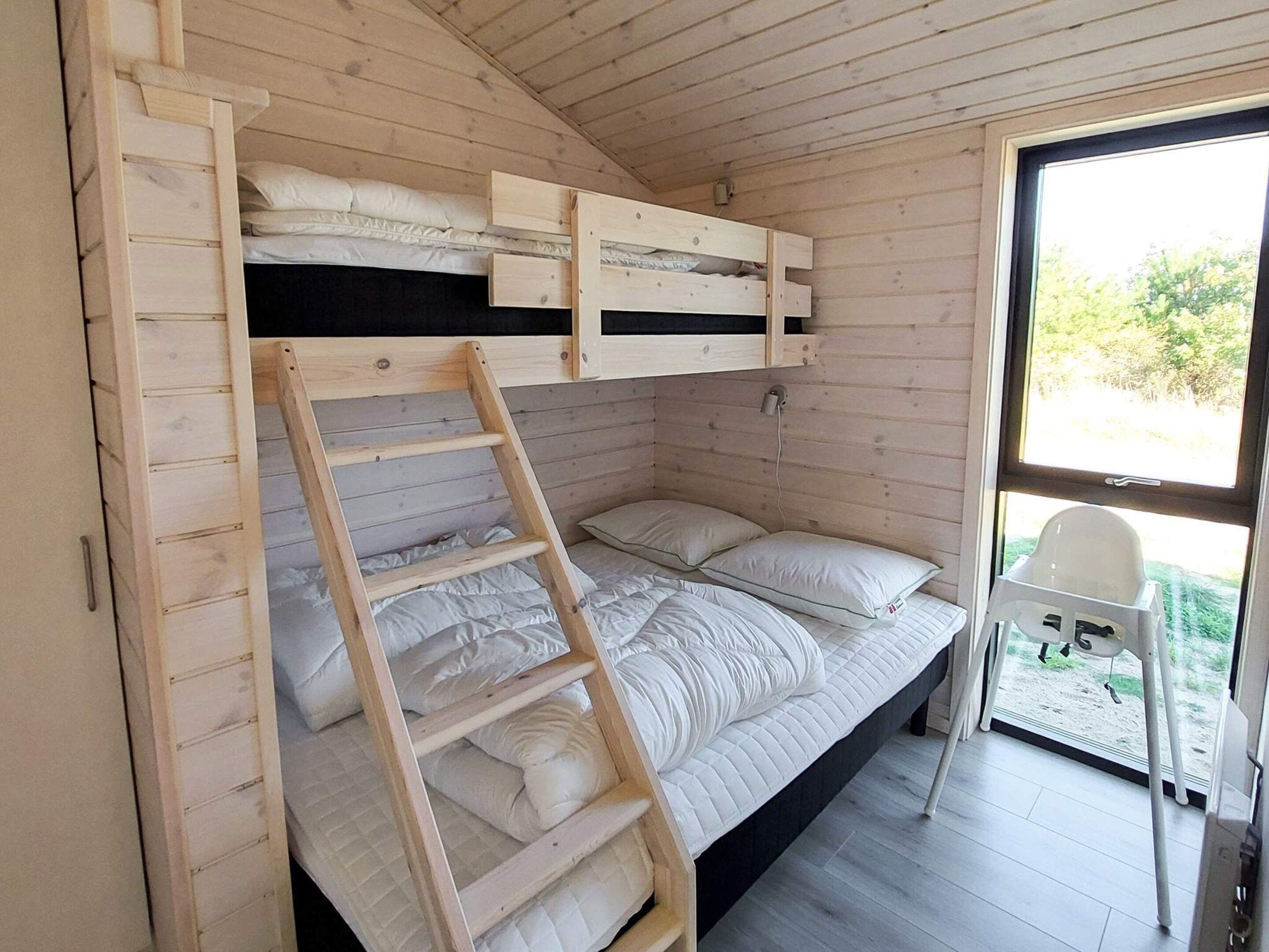 A bunk bed with a ladder, a window with a view, and a chair outside.