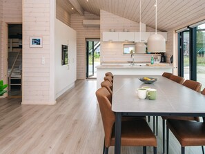 A modern kitchen with a large island, wooden flooring, and a dining area with brown leather chairs. - 5 Star Holiday Home in Romo (Rømø)