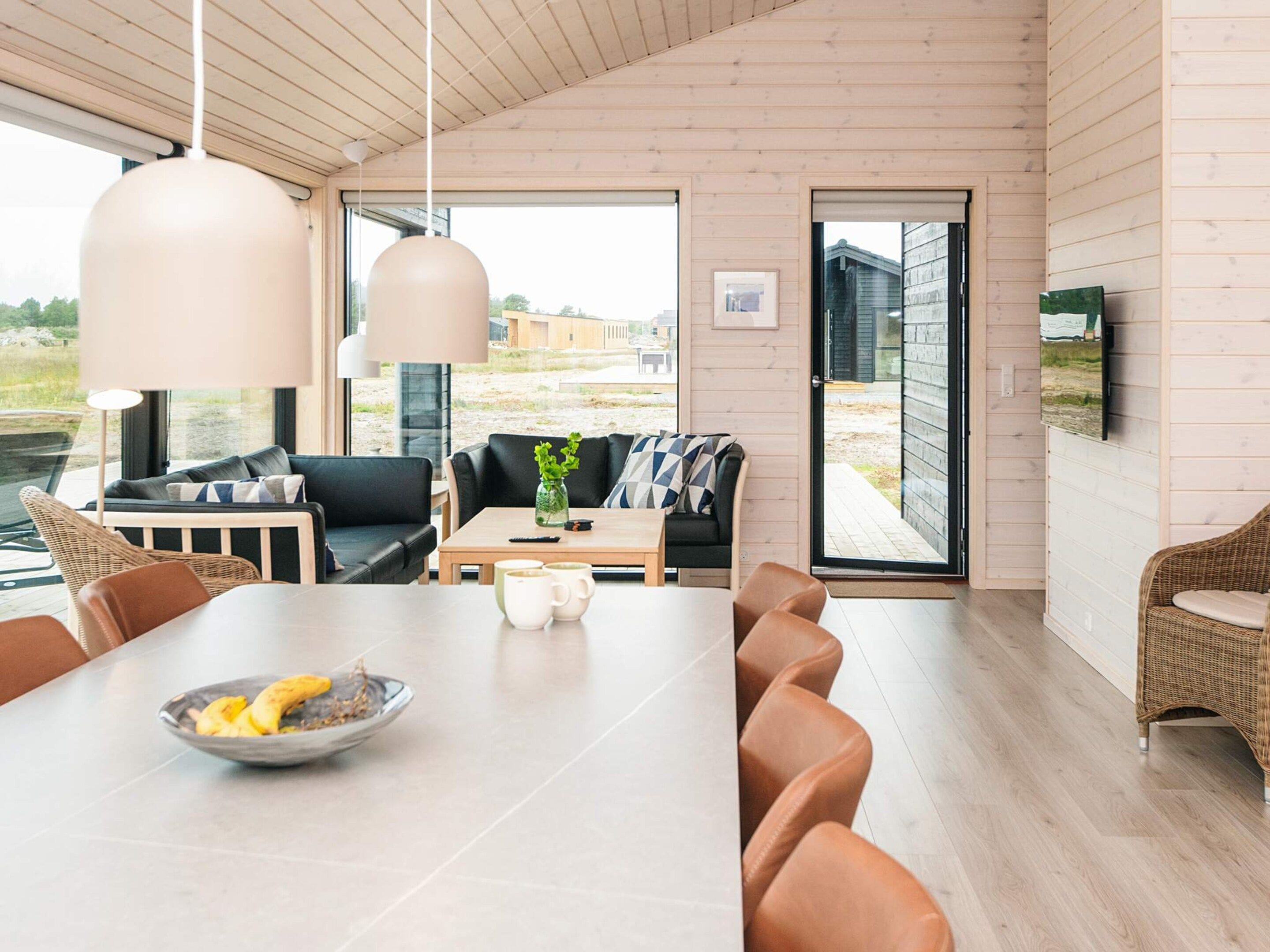 A modern interior with a wooden ceiling, a dining area with a long table, and a seating arrangement including a sofa and chairs.