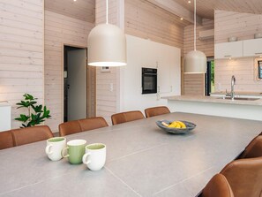 A modern kitchen with white cabinets, a built-in oven, and a large island with a bowl of fruit. - 5 Star Holiday Home in Romo (Rømø)