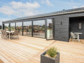 A modern outdoor deck with a dining area, a small garden feature, and a building with large glass doors. - 5 Star Holiday Home in Romo (Rømø)