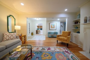 A living room with a sofa, armchair, coffee table, and a rug. There is a dining area in the background with a table and chairs.