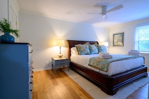 A bedroom with a wooden bed, a nightstand with a lamp, a dresser, and a ceiling fan.