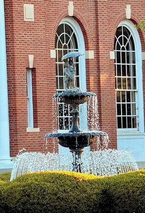 A multi-tiered fountain in front of a red brick building with arched windows.