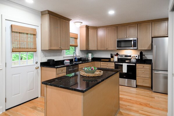 Cocina con armarios de madera, refrigerador de acero inoxidable, microondas e isla central con un cuenco decorativo.