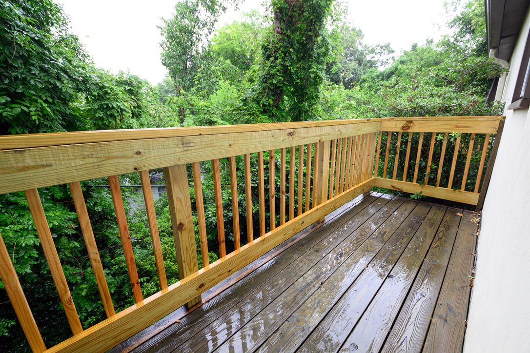 A wooden deck with a railing, surrounded by lush greenery.