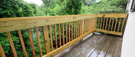 A wooden deck with a railing, surrounded by lush greenery.
