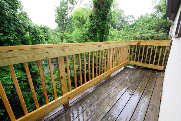 A wooden deck with a railing, surrounded by lush greenery.