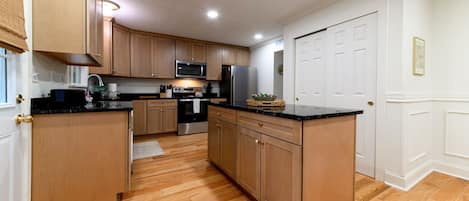 Una cocina con armarios de madera, microondas, refrigerador y lavamanos.