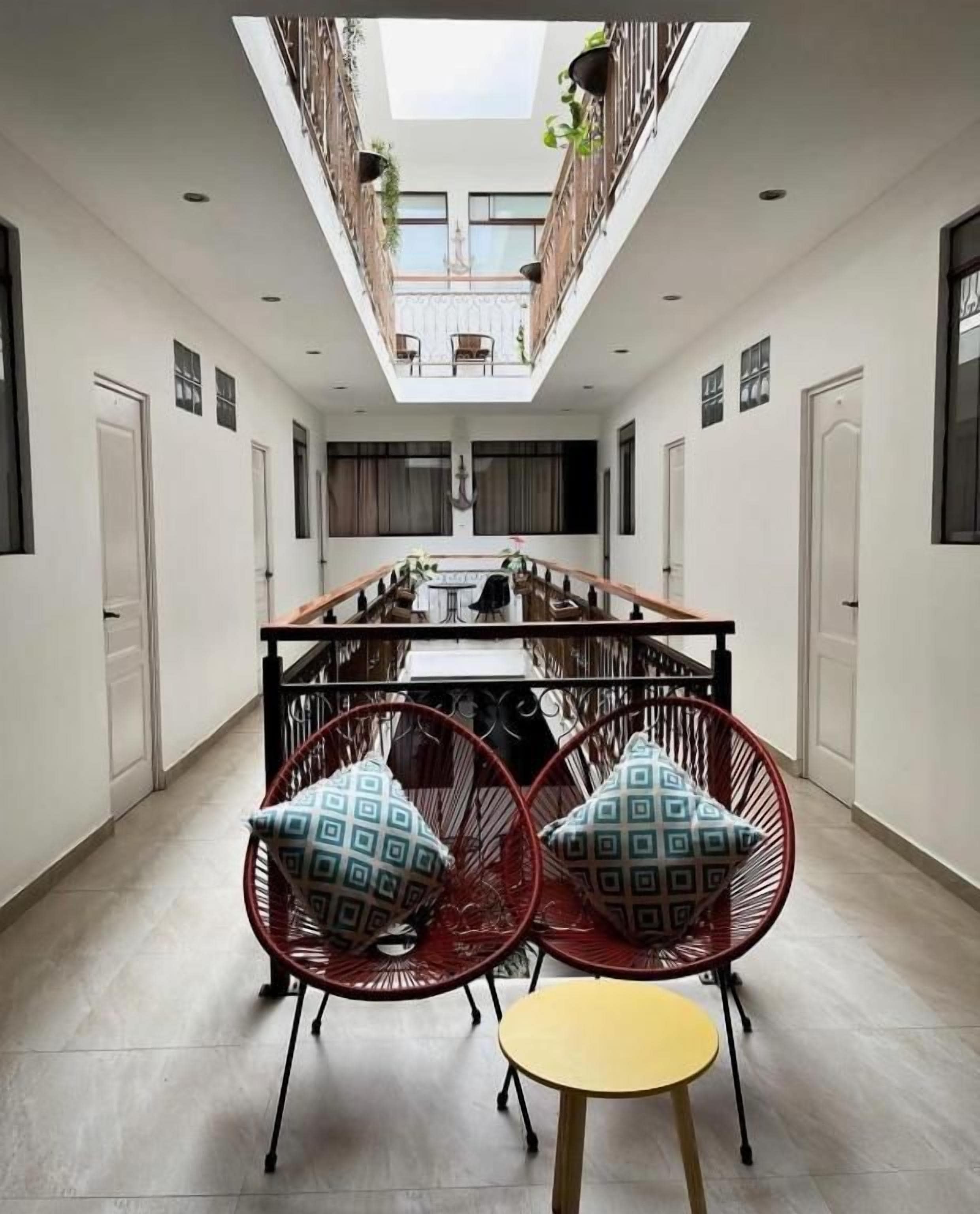 Un comedor con techo alto, una mesa central y dos sillas rojas con cojines estampados.
