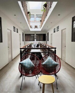 A dining area with a high ceiling, a central table, and two red chairs with patterned cushions.