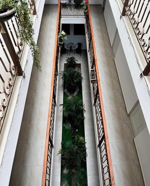 Un pasillo con una jardinera verde central, flanqueado por paredes blancas y barandales de metal.