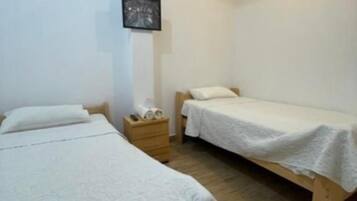 A room with two single beds, a wooden nightstand, and a small table with a lamp.