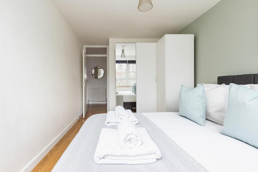 A hotel room with a bed, a bedside table, a mirror, and a view of the outside.