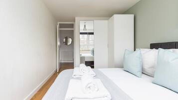 A hotel room with a bed, a bedside table, a mirror, and a view of the outside.
