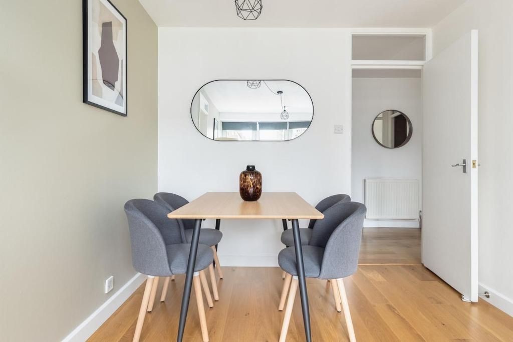 A dining area with a table, four chairs, a vase, a mirror, and a round mirror on the wall.
