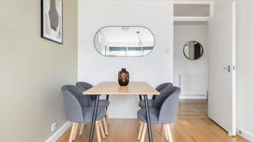 A dining area with a table, four chairs, a vase, a mirror, and a round mirror on the wall.