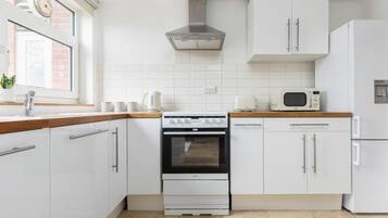 A kitchen with white cabinets, a stove, a microwave, and a refrigerator.