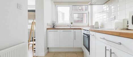 A modern kitchen with white cabinets, a wooden countertop, a built-in oven, and a window with a view of buildings.