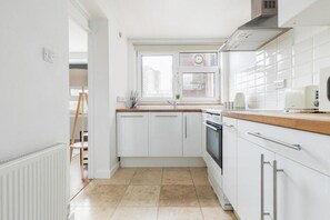 Una cucina moderna con mobili bianchi, un piano di lavoro in legno, un forno integrato e una finestra vista edifici.