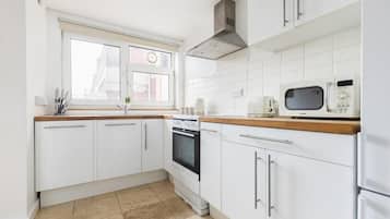 A modern kitchen with white cabinets, a built-in oven, a microwave, and a window with blinds.