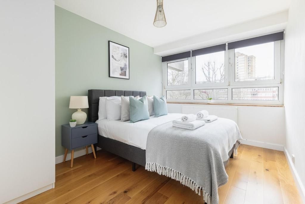 A bedroom with a bed, bedside table, lamp, and a window with a view of buildings.
