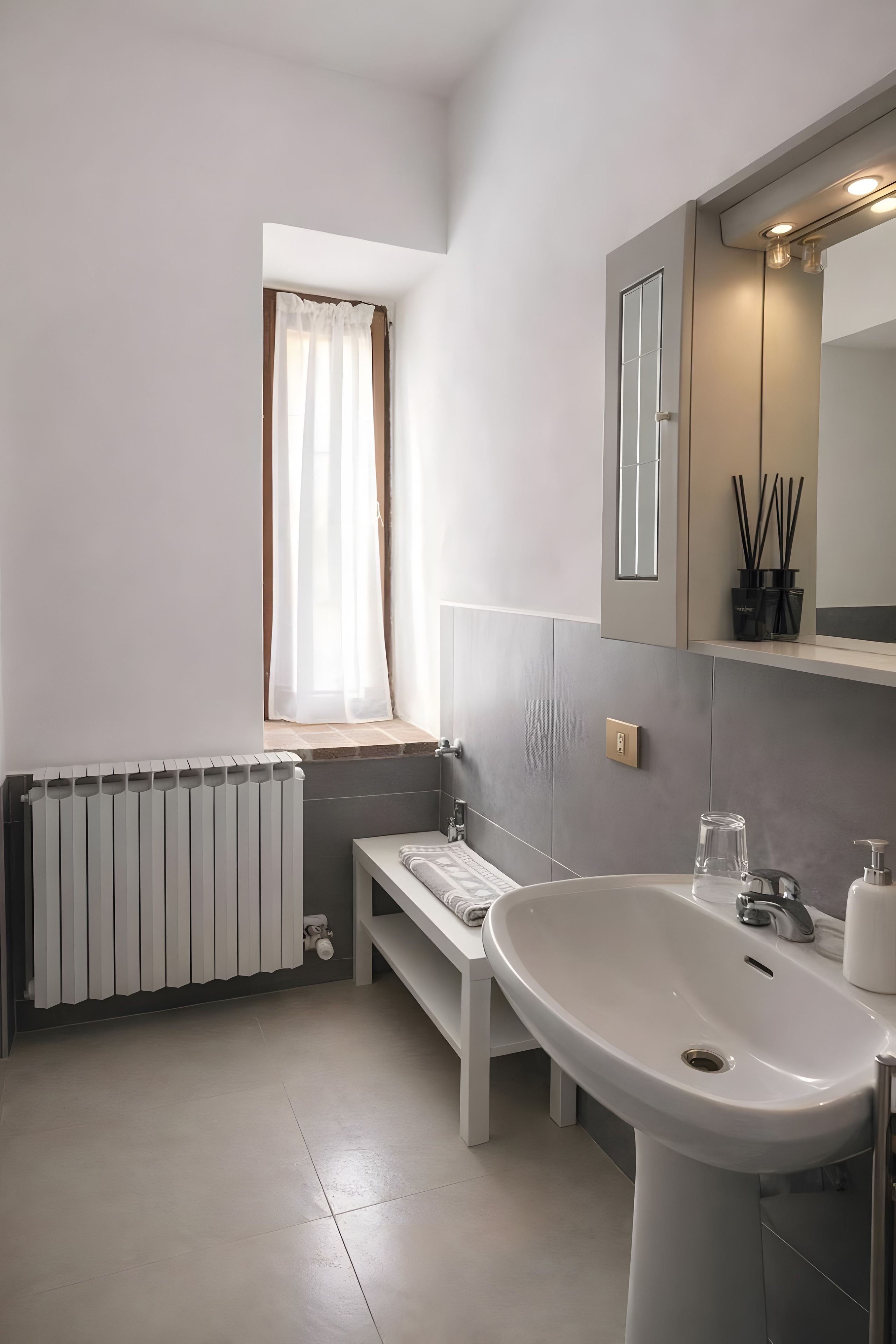 A bathroom with a white sink, a mirror, a window with a curtain, and a radiator.