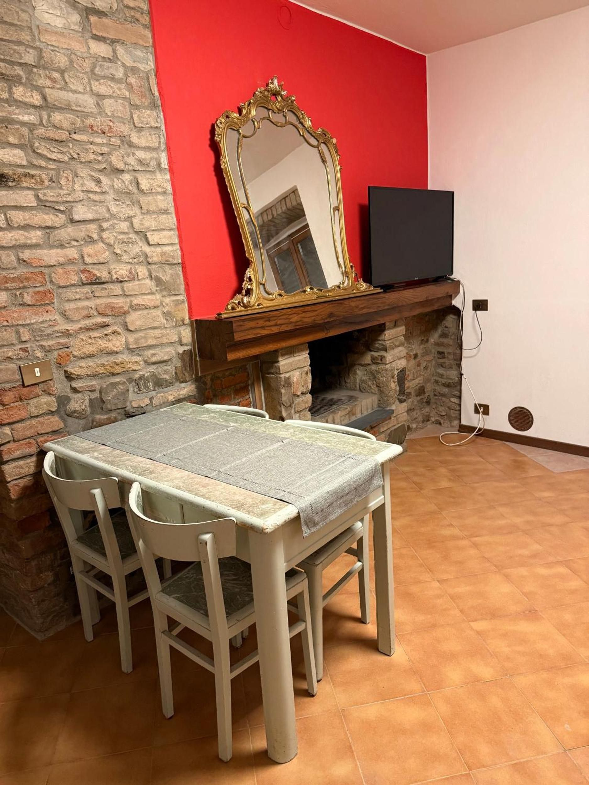 A dining area with a stone wall, a red wall, a fireplace, a television, and a table with chairs.