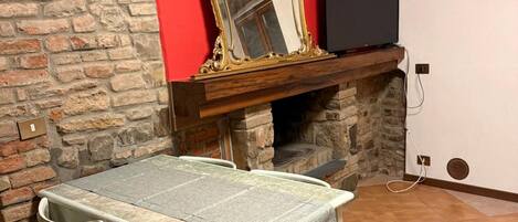 A dining area with a stone wall, a red wall, a fireplace, a television, and a table with chairs.