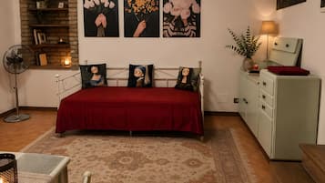 Ein Schlafzimmer mit rotem Überwurf, einem Ziegelkamin, Wandbildern, einer Nachttischlampe und einer Kommode im Vintage-Stil.