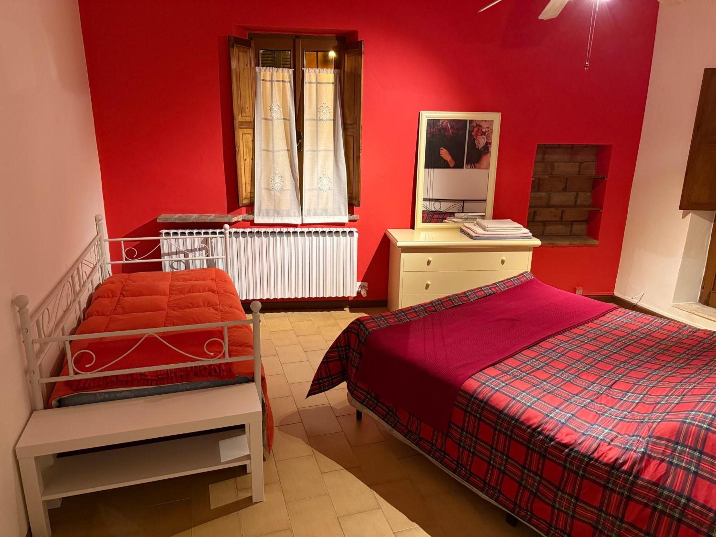 Quarto com duas camas, cómoda, radiador e janela com cortinas.