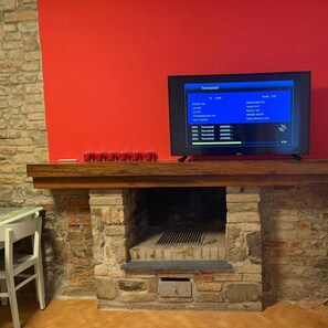 Un televisor sobre una repisa de madera frente a una chimenea de piedra, con una pared roja de fondo.