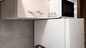 Un angolo cottura con forno a microonde, bollitore e macchina del caffè su un piano di lavoro bianco.
