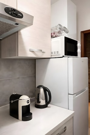 Una kitchenette con microondas, hervidor y cafetera sobre una encimera blanca.