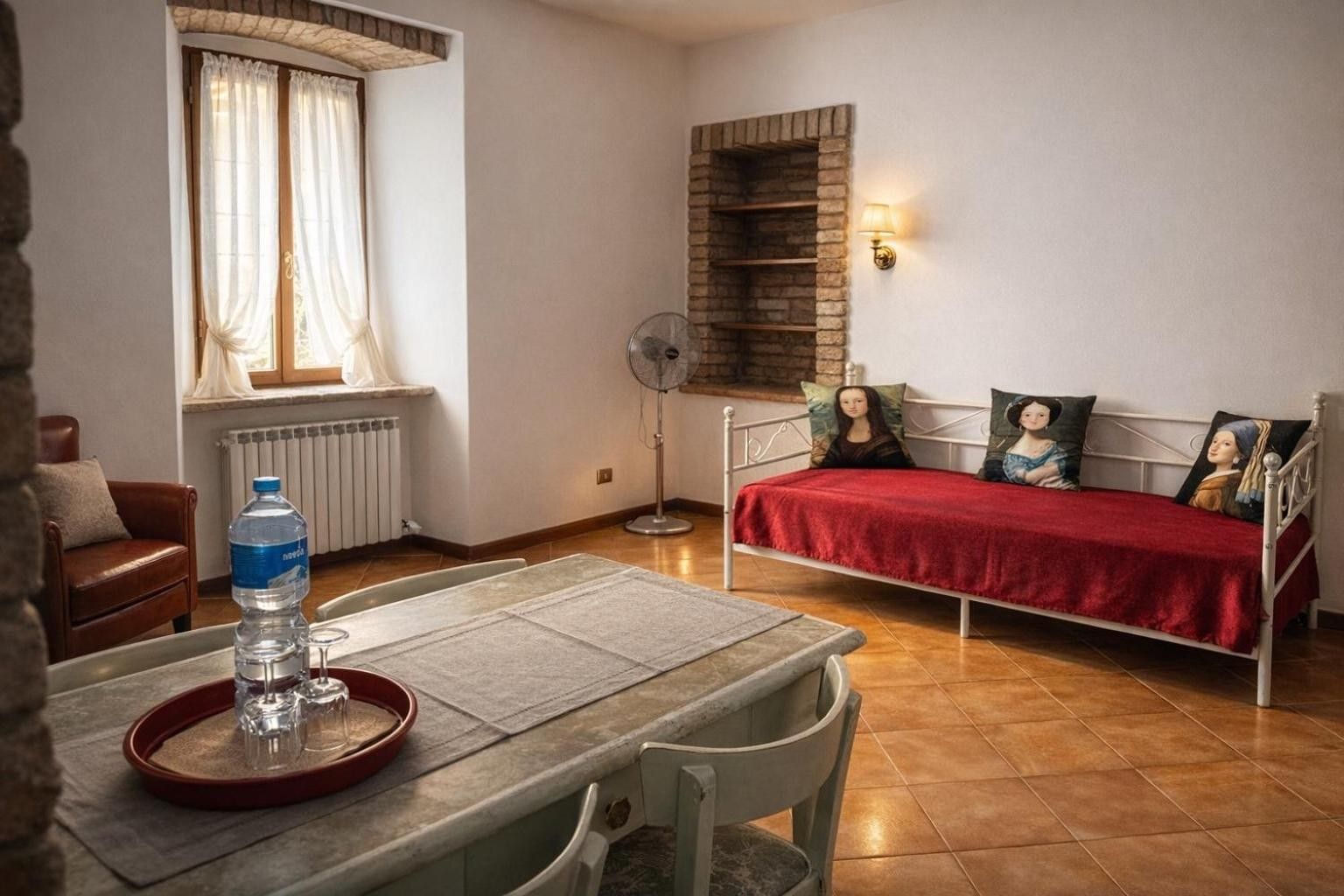 Una habitación con una cama, una mesa con una botella de agua, un radiador y una ventana con cortinas.