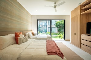 Ein modernes Schlafzimmer mit zwei Betten, einem Deckenventilator und Blick auf ein Gebäude und Grünflächen.