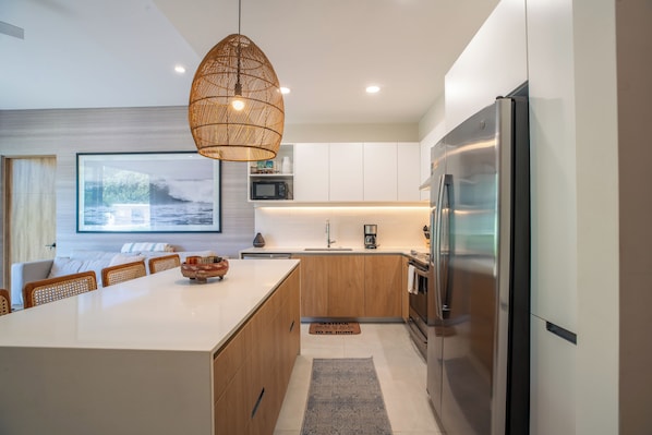 A modern kitchen with a central island, stainless steel appliances, and a hanging light fixture.