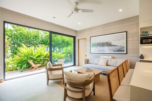 Ein modernes Wohnzimmer mit einer Couch, Sesseln, einem Couchtisch und einem großen Fenster mit Blick auf einen Garten.