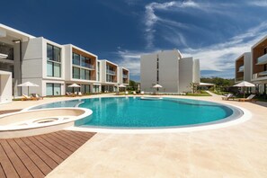 Ein modernes Hotel mit Schwimmbad, Liegestühlen und blauem Himmel.