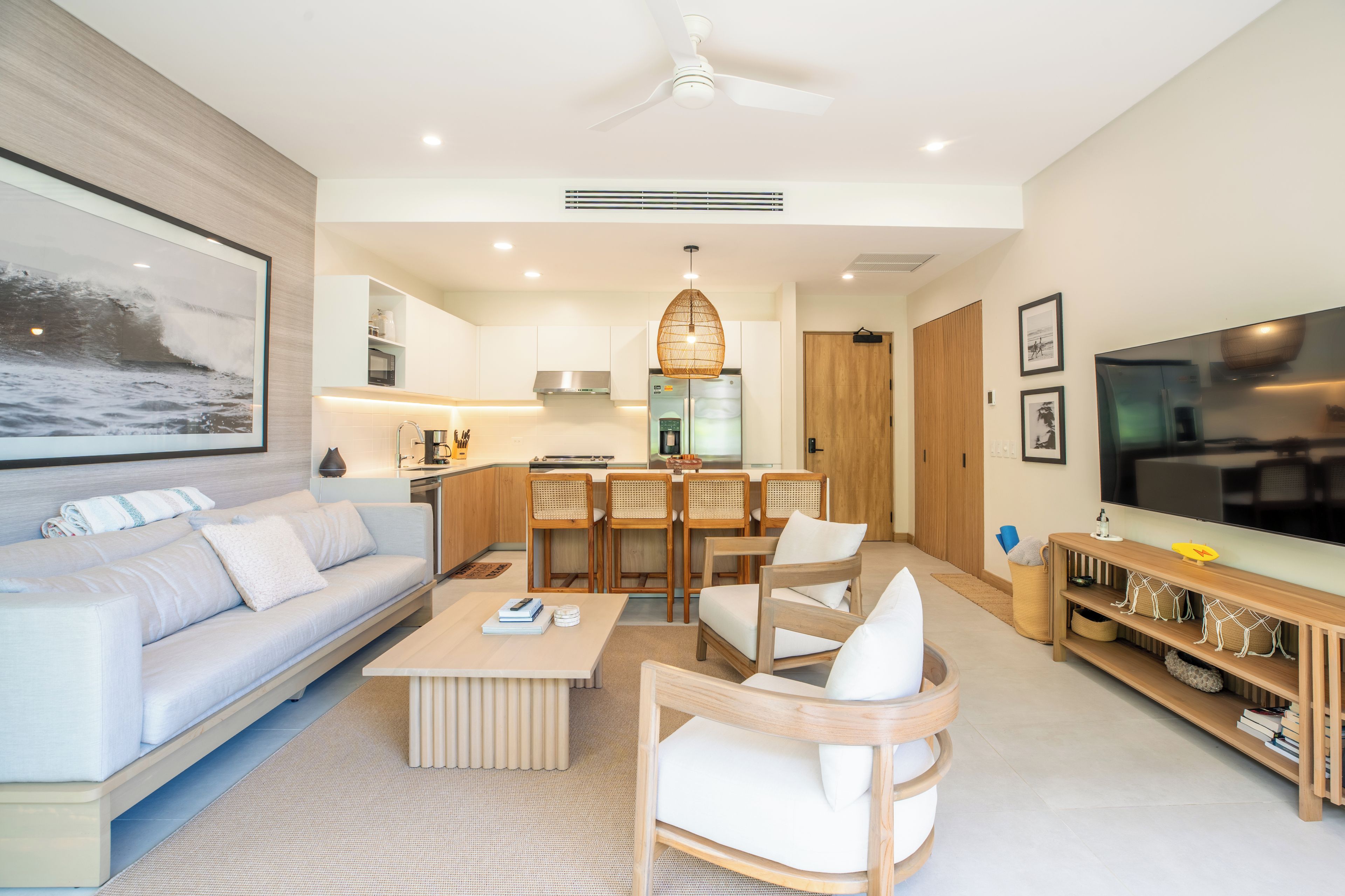 A modern living room with a sofa, coffee table, and chairs, a kitchen area with a dining set, and a flat-screen TV.