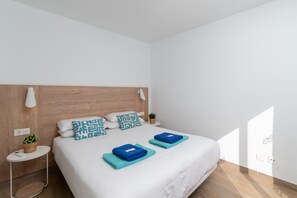 Ein ordentlich bezogenes Bett mit Holz Kopfteil, weißer Bettwäsche und zwei gefalteten Handtüchern.