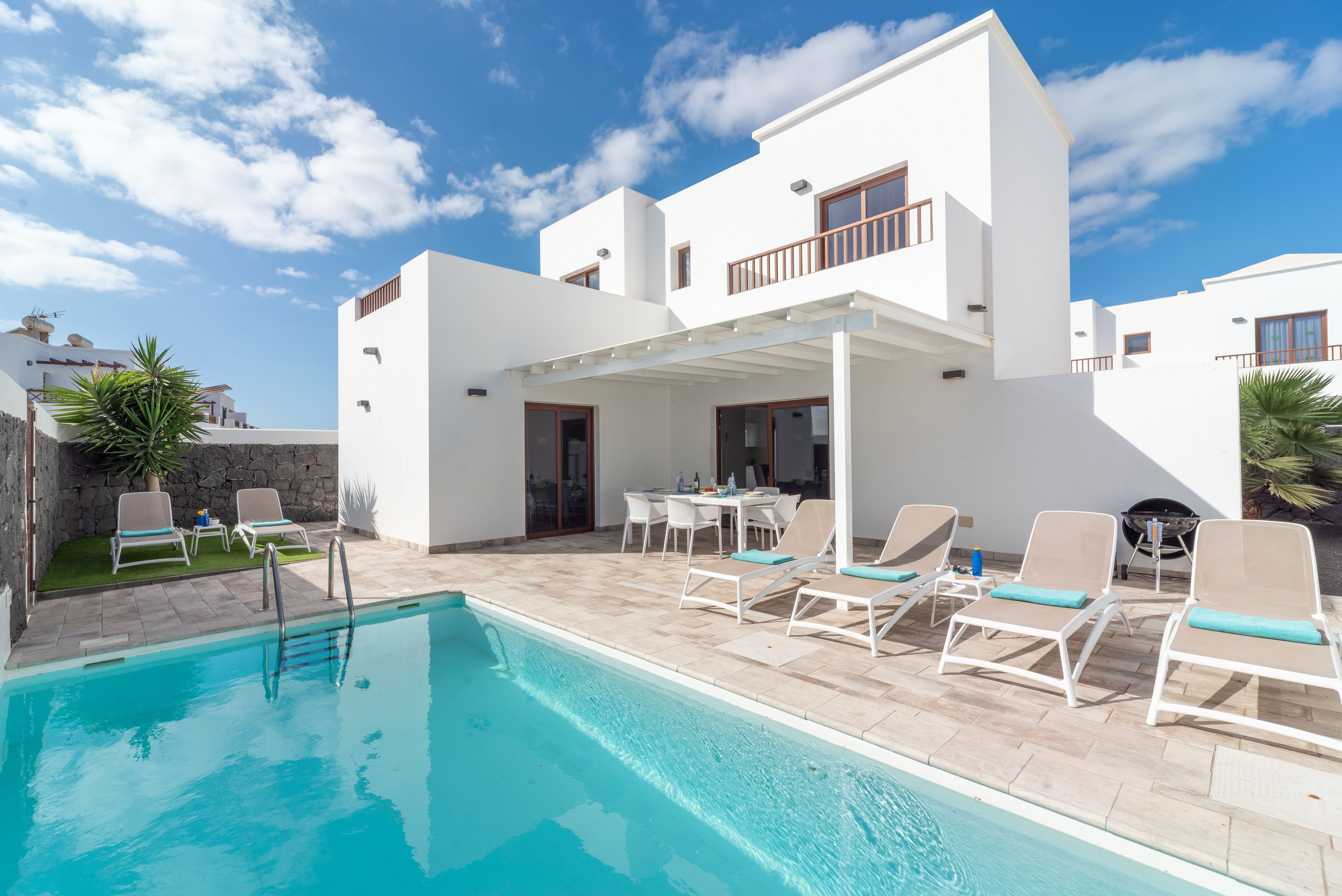 En moderne villa med swimmingpool, udendørs møbler og en overdækket terrasse.