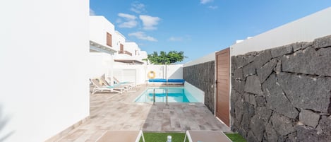 A pool area with lounge chairs and a small table with a towel and fruit.