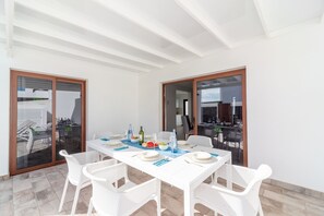 Ein Essbereich mit Tisch für vier Personen, weißen Stühlen und Blick durch Glasüren auf eine Außenpatio.