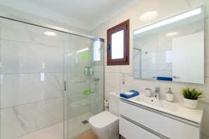 Een moderne badkamer met een douchecabine van glas, een toilet, een wastafel met spiegel en een kleine potplant.