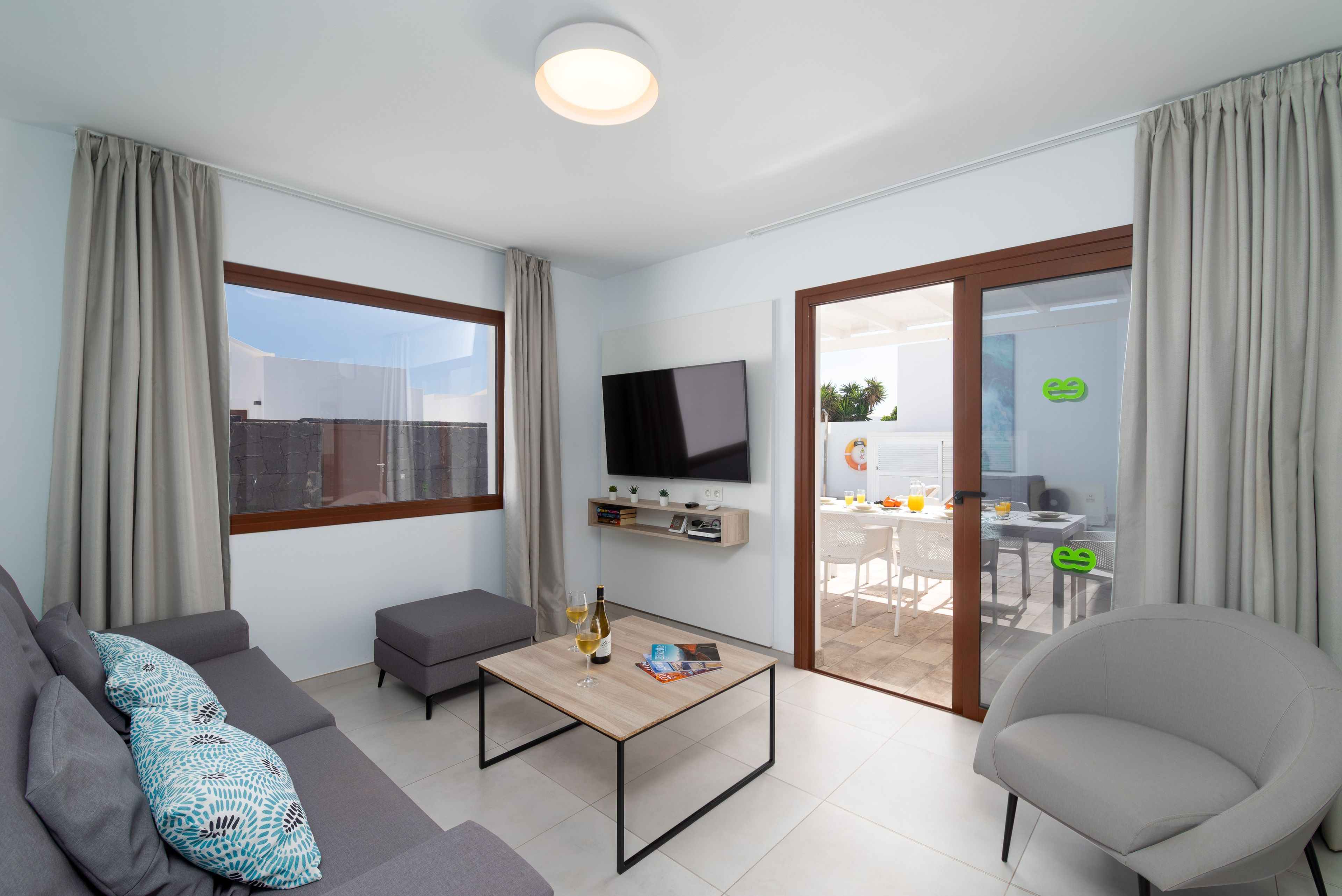 Un salon moderne comprenant un canapé, une table basse, un téléviseur fixé au mur et une porte-fenêtre coulissante donnant sur un espace extérieur.
