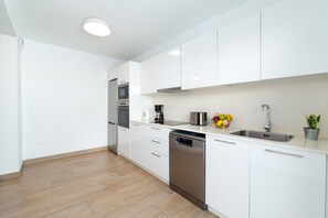 A modern kitchen with white cabinets, stainless steel appliances, and a wooden floor. - Ereza Villas La Granja – 3-Bedroom Villas with Private Pool in Playa Blanca (Yaiza)