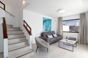 Ein modernes Wohnzimmer mit Treppe, einem grauen Sofa, einem Couchtisch und einem großen abstrakten Gemälde.