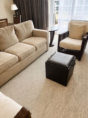A hotel room with a sofa, a chair, a small table, and a lamp.